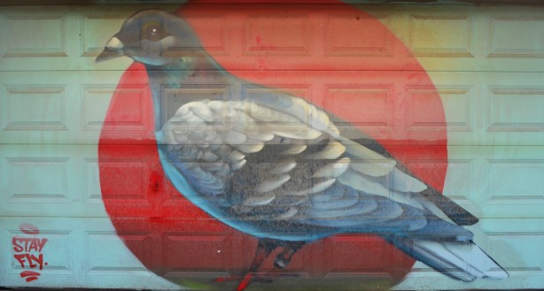 a large painting of a pigeon on a garage door in an alley 