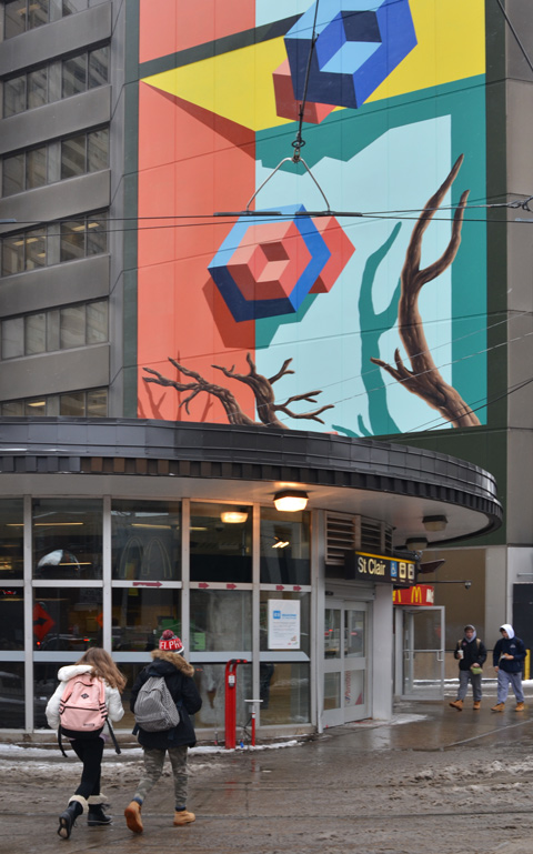 street entrance to St. Clair subway station, some people walking towards it, a large mural on the building behind it