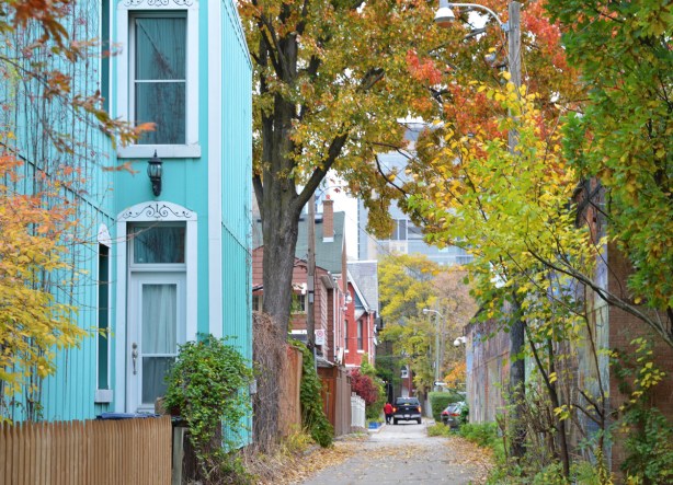 part of a tuquoise painted house beside an alley with fall foilage, a truck and man in the distance