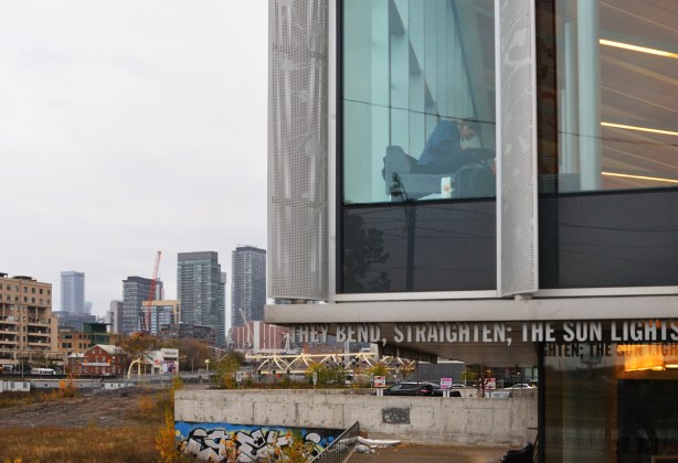 a person works at a table beside the window in a library, building sticks out, railway tracks and yard below, with highrises in the background