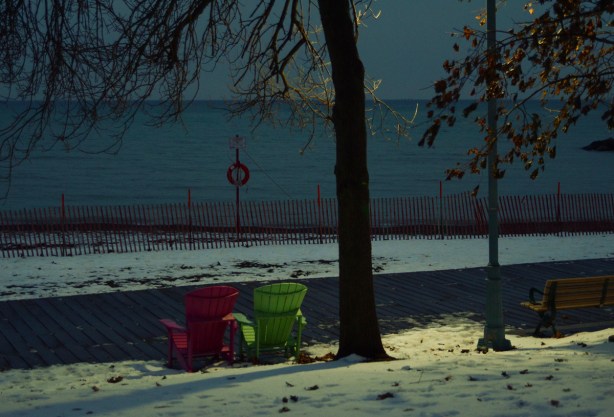 after dark, lights shining on two Muskoka chairs beside the boardwalk at Kew Beach 