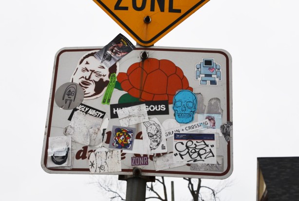 many stickers on a traffic sign, including rob ford's face and a blue skull