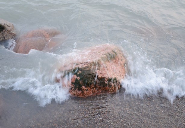 slow mo pic of waves crashing over a rock at the beach