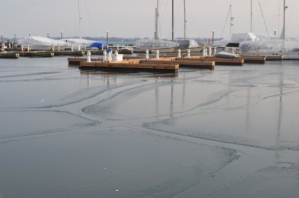 a couple of boats docked at wood docks, lakefront, waterfront, some thin ice in patches on the water between the shore and the boats. Lake Ontario 