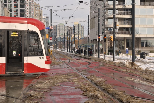 new TTC streetcar turning left from Spadina to Queens Quay, slushy streets after snowfall, people waiting at bus stop, 