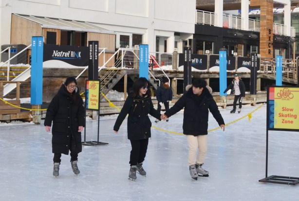 three people skating at an outdoor skating rink
