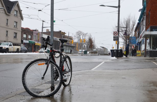 a bike with a flat front tire is locked to a street sign pole on the sidewalk on St. Clair west