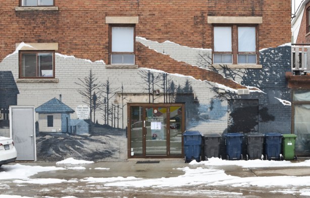 mural in blues and greys on the side of a brown brick building, an outdoor winter scene