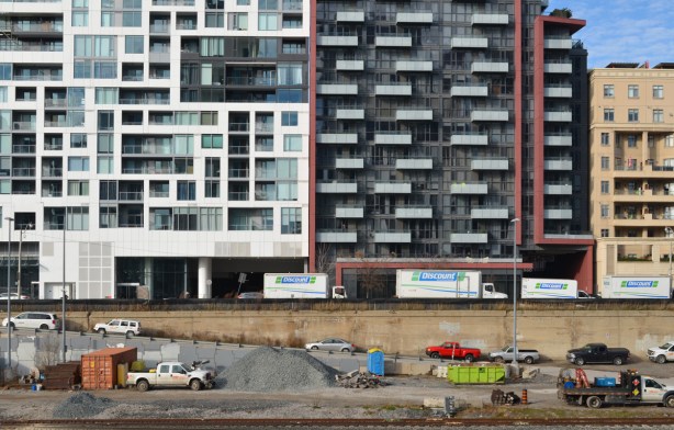 a line of glass and concrete condos on Front street that face the railway tracks, cars and trucks at construction site beside the tracks, below street level 