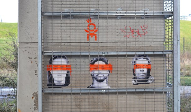 graffiti, three black and white photos of faces with orange streak painted through their eyes, pasteups on concrete 