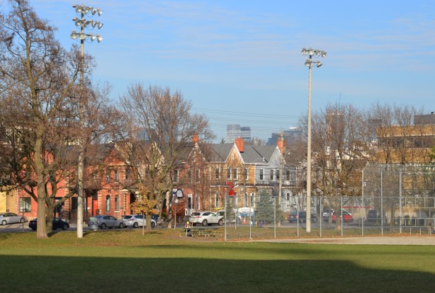 park, green space, baseball diamond with lights, and a row of bright coloured houses behind