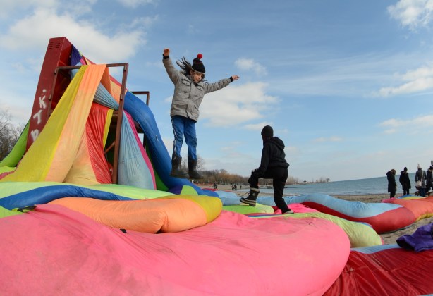 a girl jumping off a lifeguard station onto rolls of fabric stuffed with straw, on the beach 