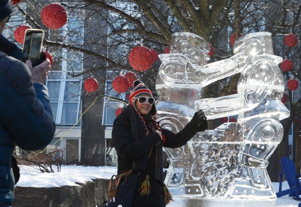 a woman in a winter hat with the Union Jack on it, pointing at an ice sculpture while a man takes her picture