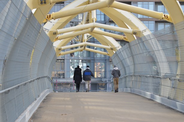 three people crossing the puente de luz, the yellow pedestrian bridge that crosses the railway tracks 