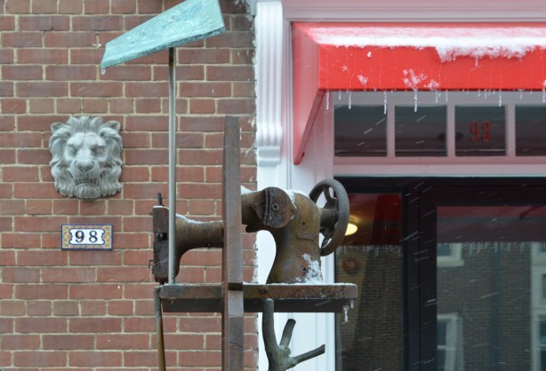 little metal sculpture of a sewing machine on a pole with a bit of green above it
