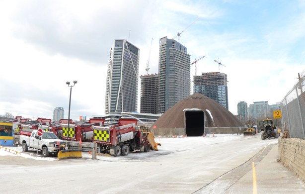 parking lot for red snowplows, city property, also a dome shaped storage for sand, condos in the background