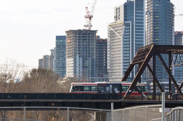 TTC streetcar passes over Bathurst street bridge over the railway tracks, new condos in the background, crane