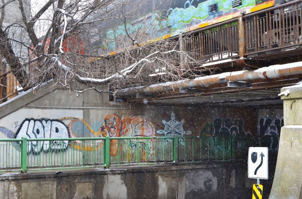 train with grafiti on the side of the car passes over a bridge over Dufferin Street and there is graffiti on the walls of the underpass
