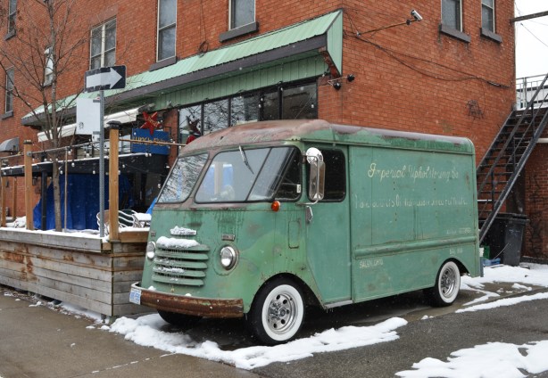 old green Chevrolet delivery van with Imperial Upholsteriing Co written in faded cursive writing on the side