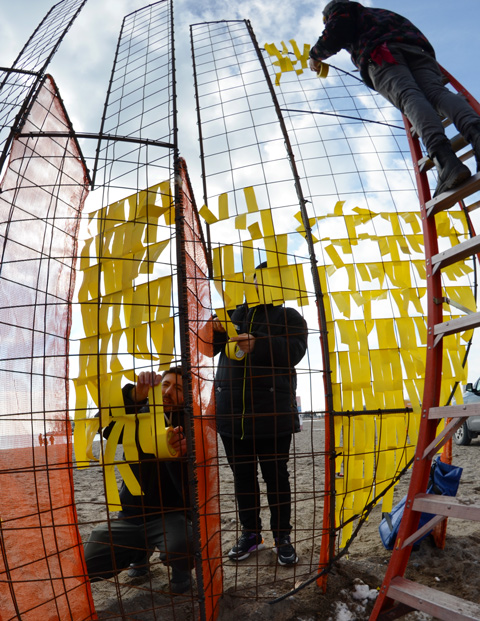tying yellow ribbons on an orange metal frame, finishing touches on an art installation called Mirage 