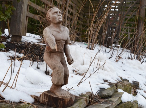 a small wooden carving of a man with a broken arm, outside in the snow 