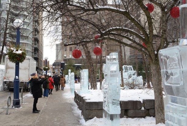 Cumberland Ave decorated for the IceFest, red balls hanging from trees, ice sculptures on display beside the sidewalk, a few people looking at them