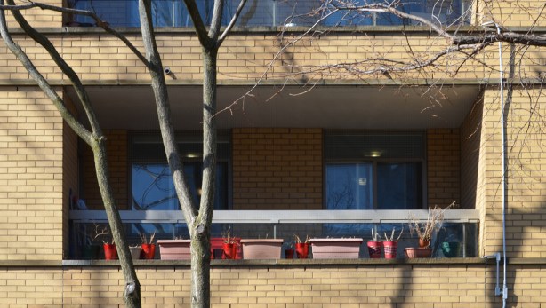 a row of pink window boxes and red planters on a balcony of a yellowish brick apartment building