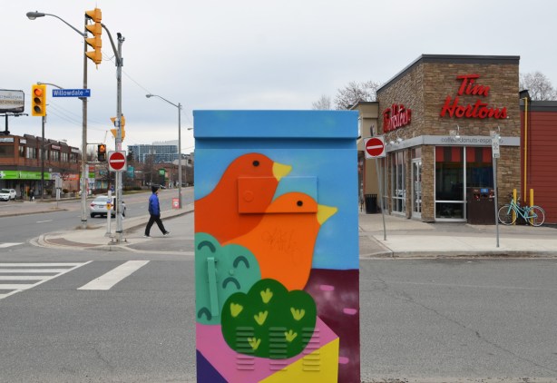 a street box painted with a red bird and an orange bird in green bushes, Tim Hortons behind as well as street scene at Willowdale and Sheppard Ave East 