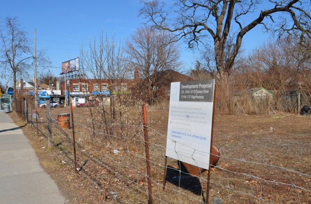 vacant lot on the corner of O'Connor and Pape, with fence around it, development proposal sign from 2014, overgrown, 