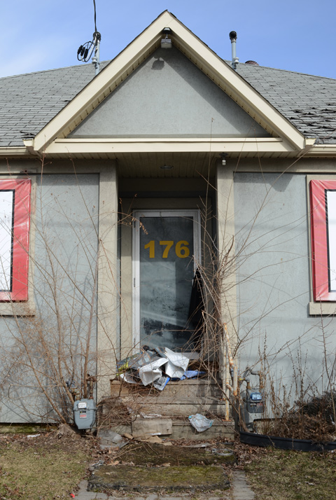 front door of abandoned building at 176 Sheppard Ave East with collection of garbage on overgrown front step