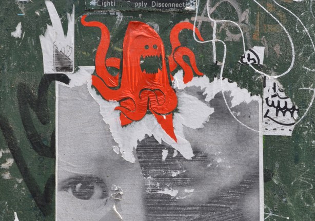street art black and white pasteup of a face with eye still showing, torn a bit, sticker of a red octopus on top of the head 
