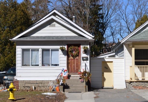 white bungalow with Christmas wreath on brown wood front door and a santa claus decoration on the front steps, a yellow fire hydrant by the sidewalk