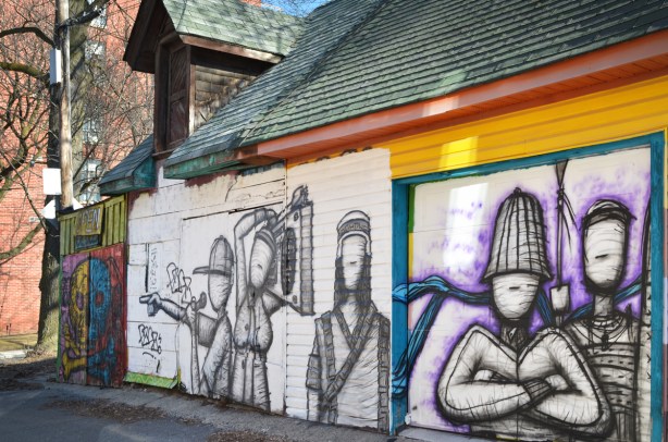 black drawings on white, large street art covering the side of a building, faceless people, singer, microphone, man with arms folded,