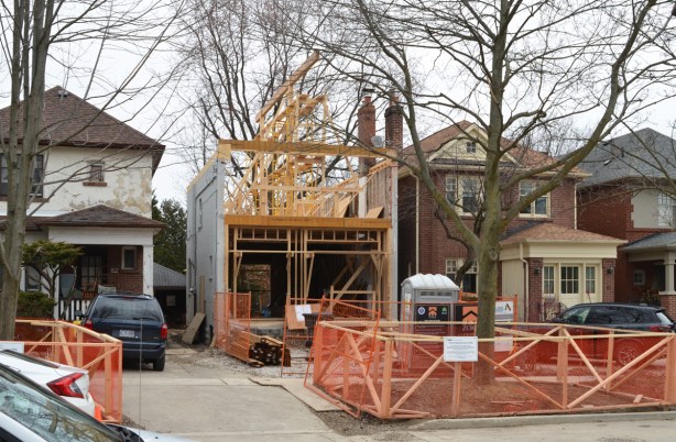 three older houses on a street, the one in the middle has been gutted to the other walls, side only, open roof, new beams beinginstalled for a third storey