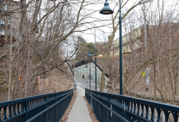 a man jogging past concrete wall and elementary school, at bottom of ramp to pedestrian bridge, street lamp above the ramp