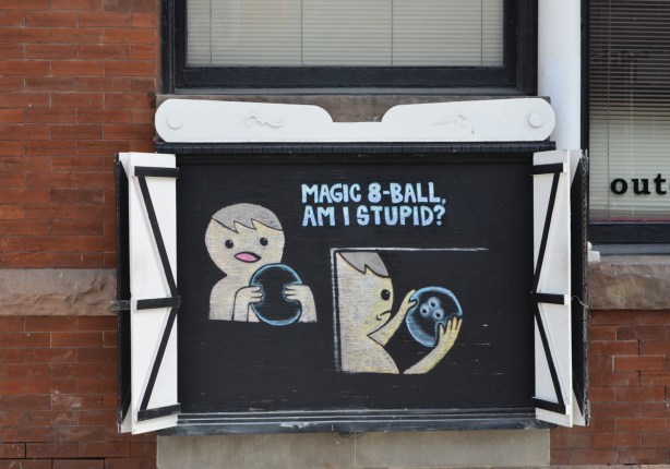 drawing on chalkboard outside, man asking magic ball am I stupid, then he realizes ball is really a bowling ball 