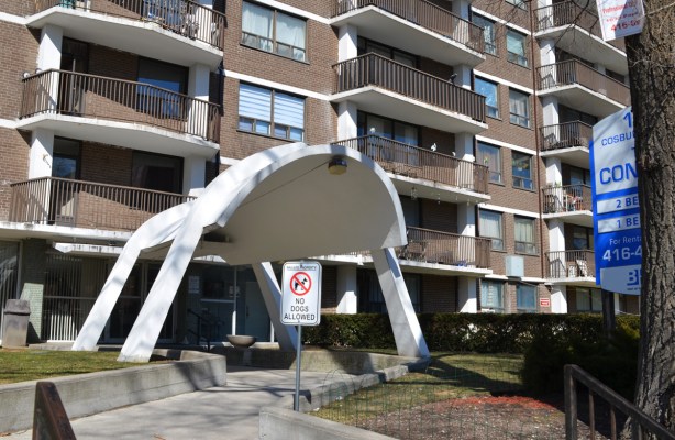 curved white concrete cover over entrance of apartment building, that is brown brick with white balconies