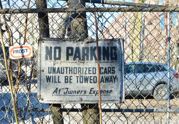 very old no parking sign on a chain link fence 