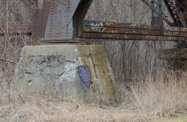a purple graffiti heart painted on the concrete support at the bottom of a large metal trestle