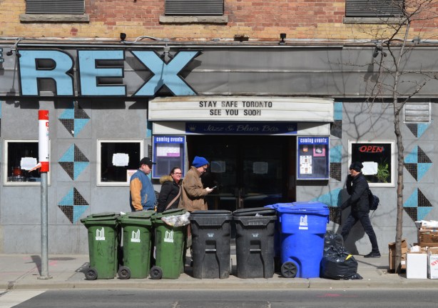 people walking past the Rex on Queen Street, has sign over door that says