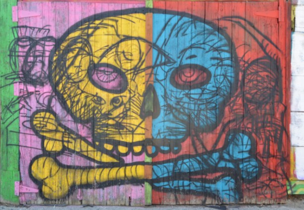 old wood garage door with street art of a skull and cross bones in bright colours, yellow, pink, blue, and orange