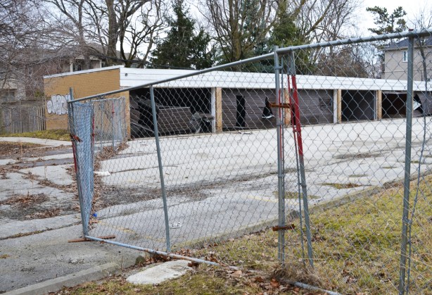 metal wire fence around an empty parking lot and row of garages with broken brown doors 