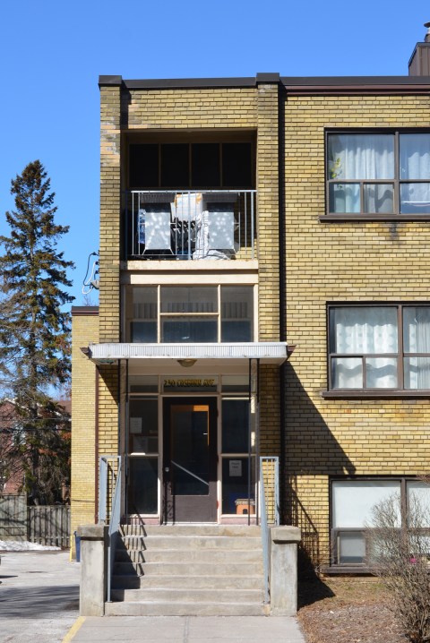 front entrance, exterior, of a yellow brick lowrise apartment building from the 1960s or 1970s