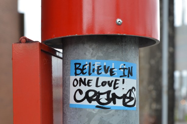 a sticker on a ttc bus stop pole that says believe in one love