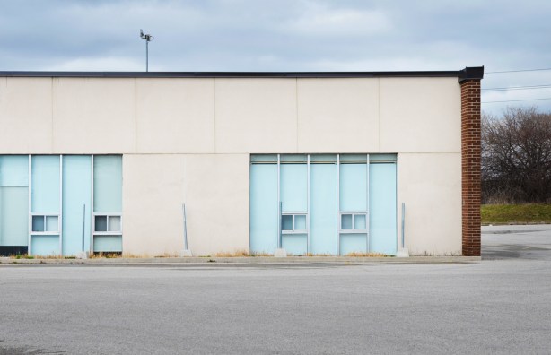 low one storey building with two large windows with blinds closed, no cars in parking lot 