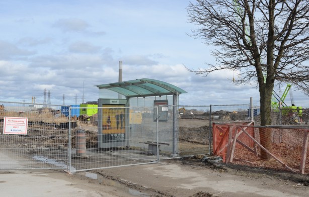 a glass bus shelter behind a construction fence 