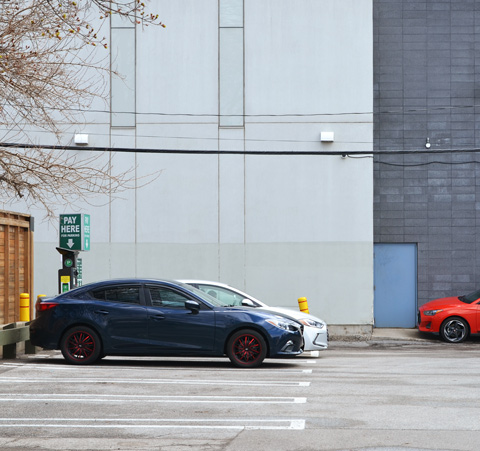 building beside a parking lot with three cars parked there, white car, blue car and red car
