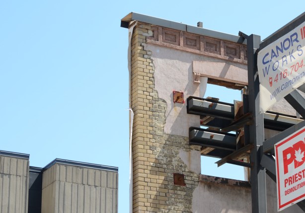 corner of a facade being saved during construction, old brick and detail work, window with no glass, showing metal supports keeping the wall up 