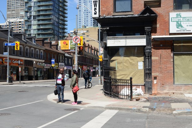 s couple standing on a corner on Yonge street waiting for a light to change, and talking 