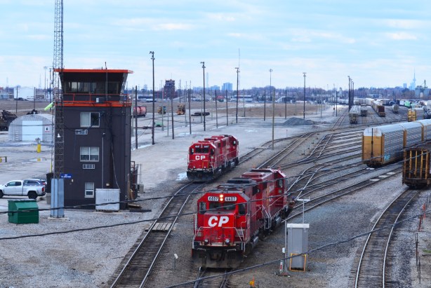 seen from a bridge, two bright red CPR train engines on tracks, beside the watch tower